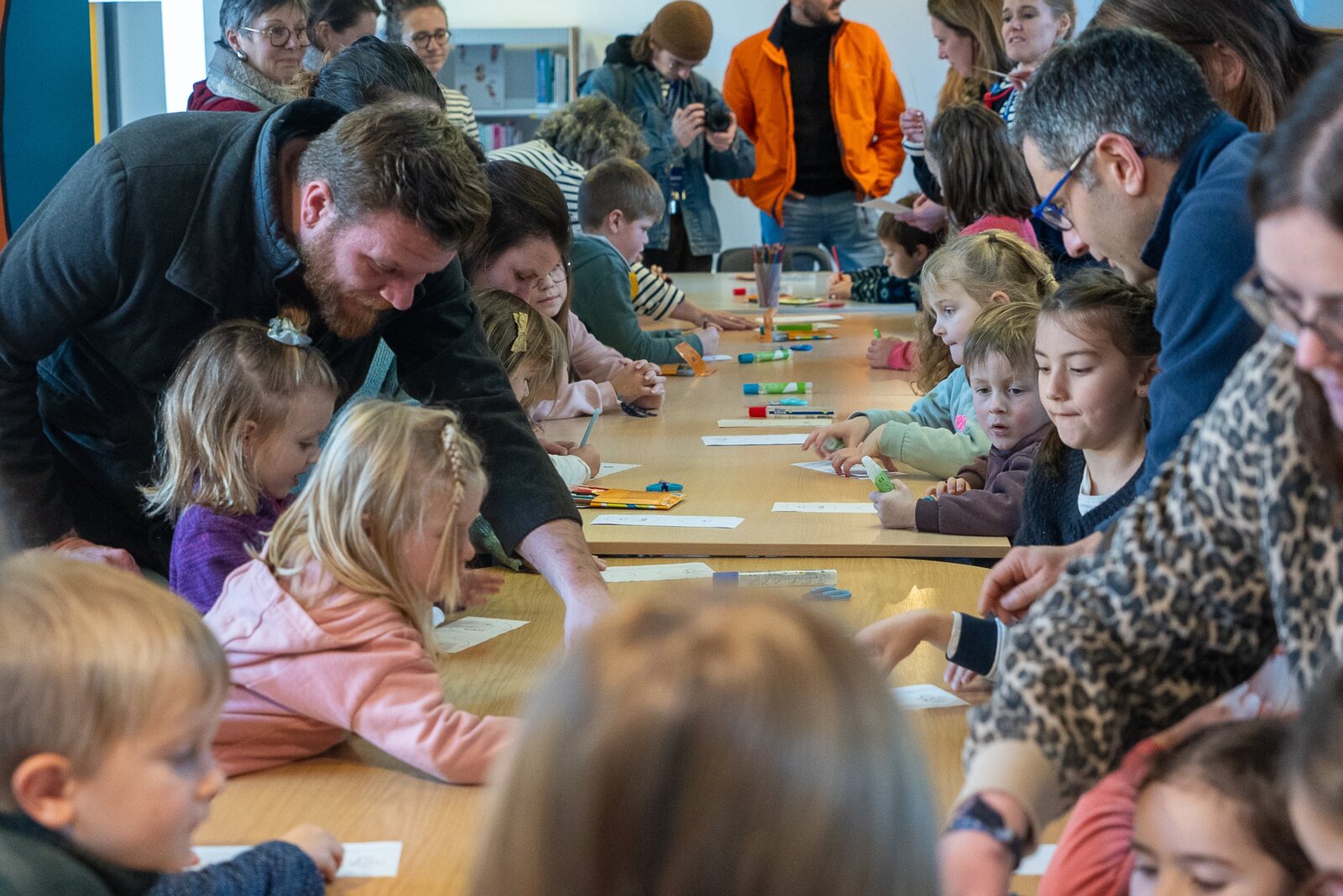 Des enfants et leurs parents autour d’une grande table pendant un atelier créatif des P’tiots Égalués, à la médiathèque de Carentan